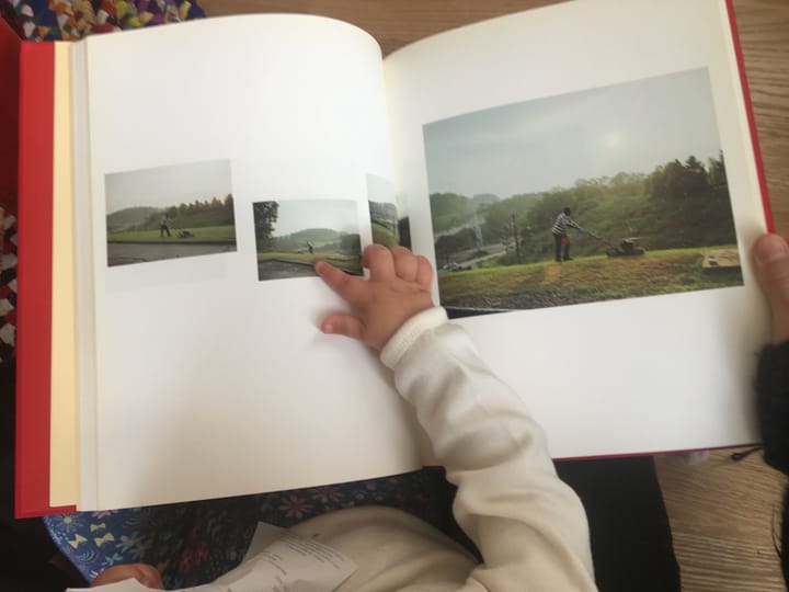 Looking at a photo book a child in my lap. A sequence of images show a man mowing a grassy hill.